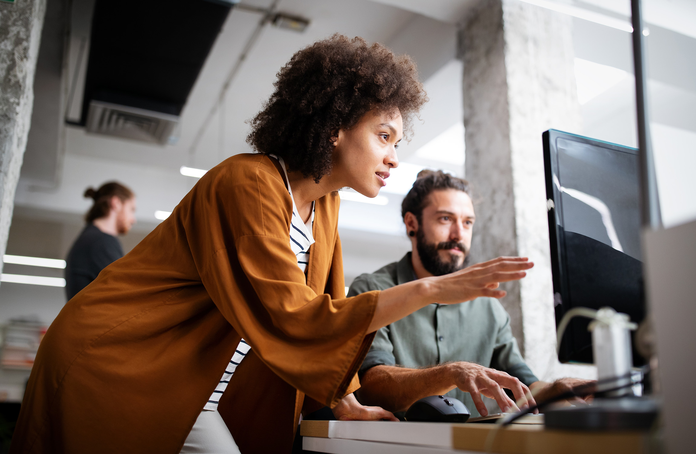 Colleague pointing at a computer screen while helping a teammate