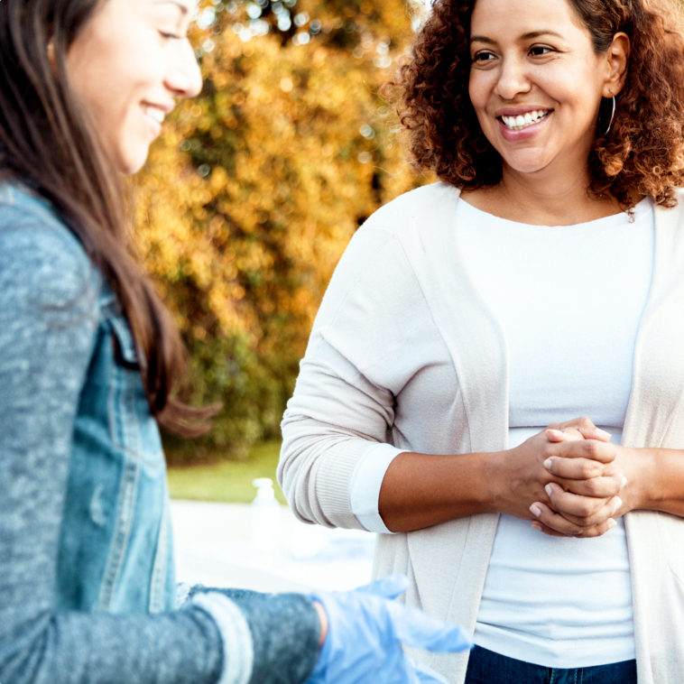 Two women smiling together at an outdoor volunteer event